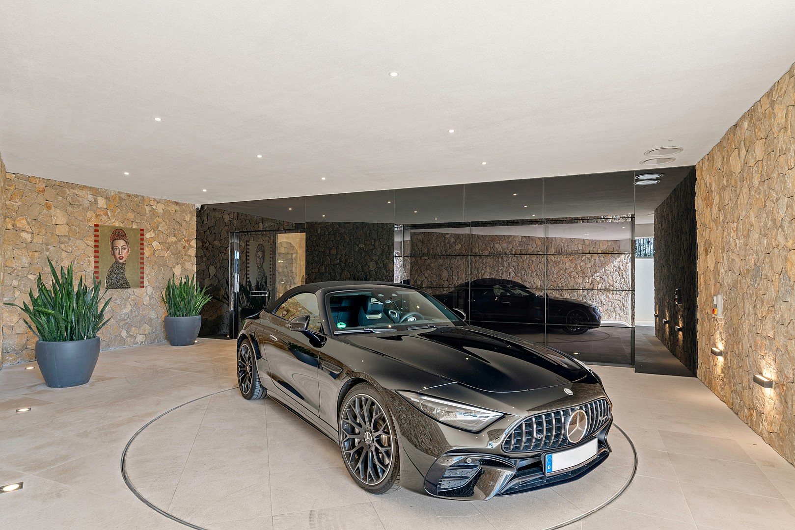 A luxury garage interior featuring a dark sports car on a mechanical turntable, flanked by natural stone walls and planters.