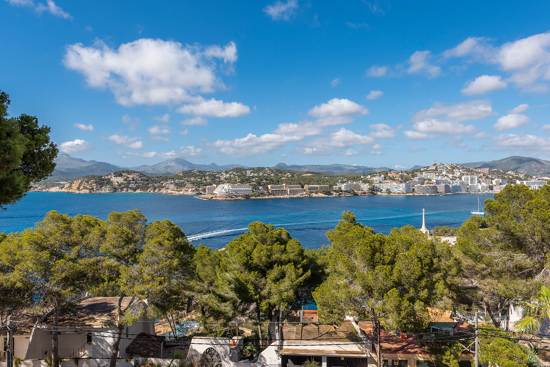 Elevated view overlooking a blue bay, forested coastline, and distant mountains under a clear sky.