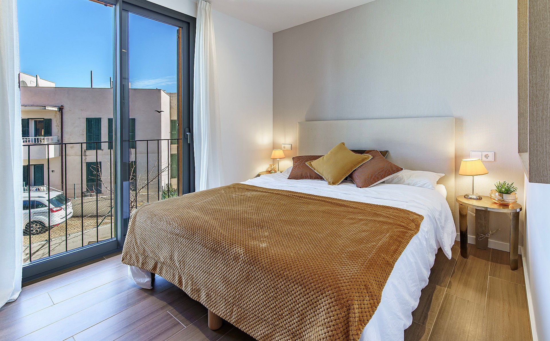 A contemporary bedroom with a double bed, brown patterned throw, and a sliding glass door opening to a small balcony.