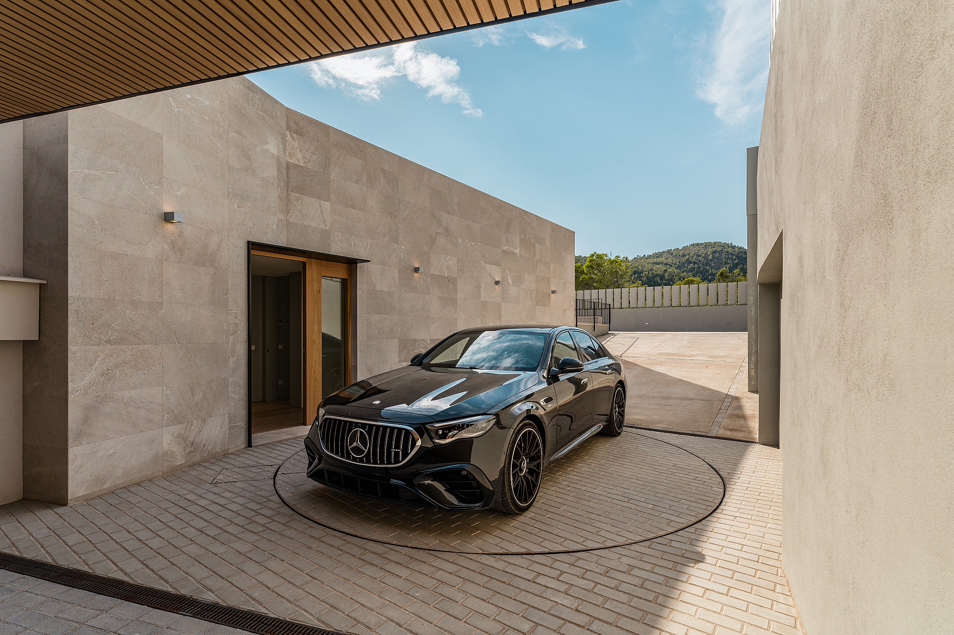 A black sedan parked on a circular metal turntable within a stone-walled courtyard under a bright blue sky.