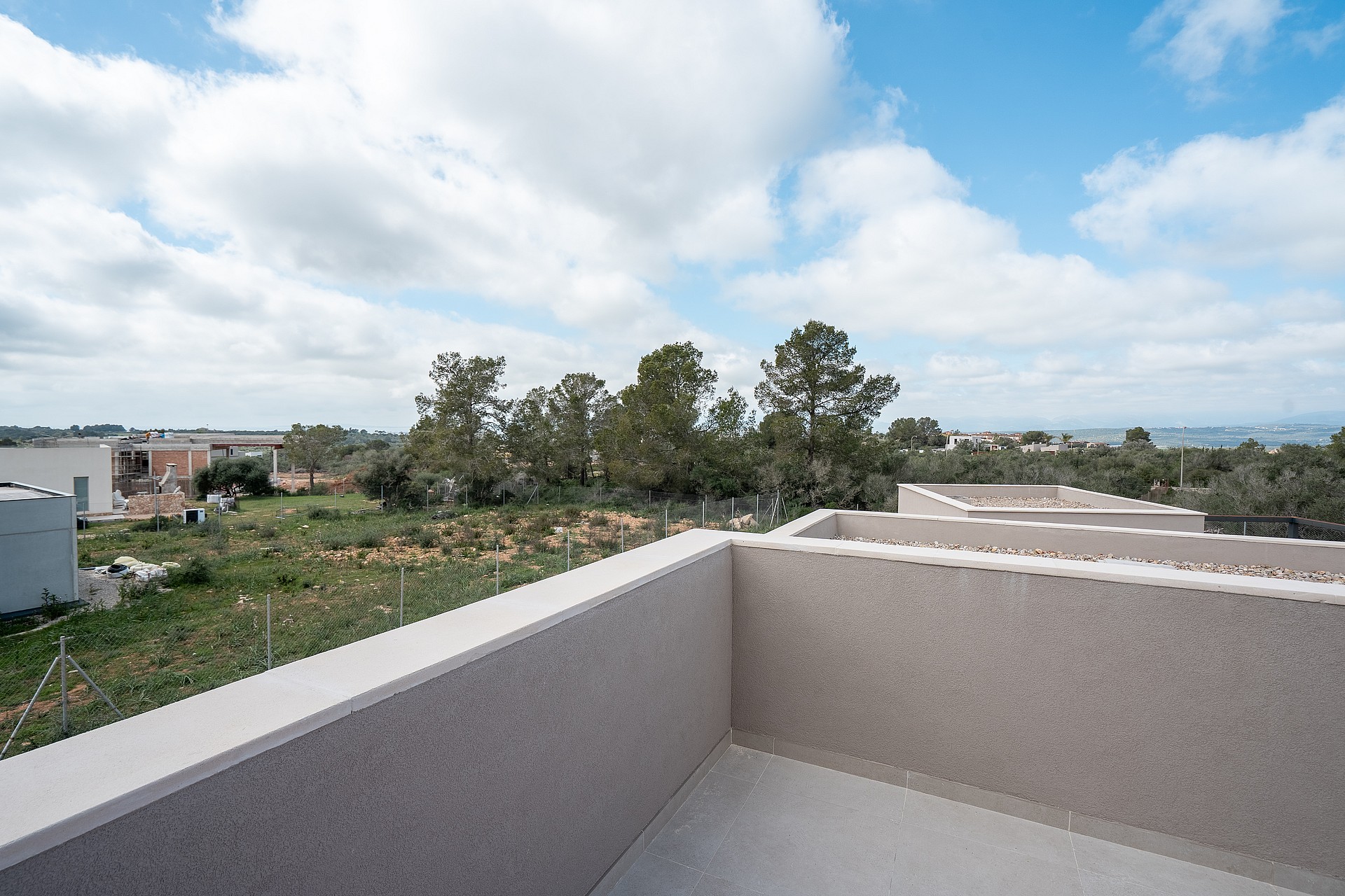 A wide angle view from a minimalist terrace with stone parapets overlooking a landscaped garden and distant mountains.