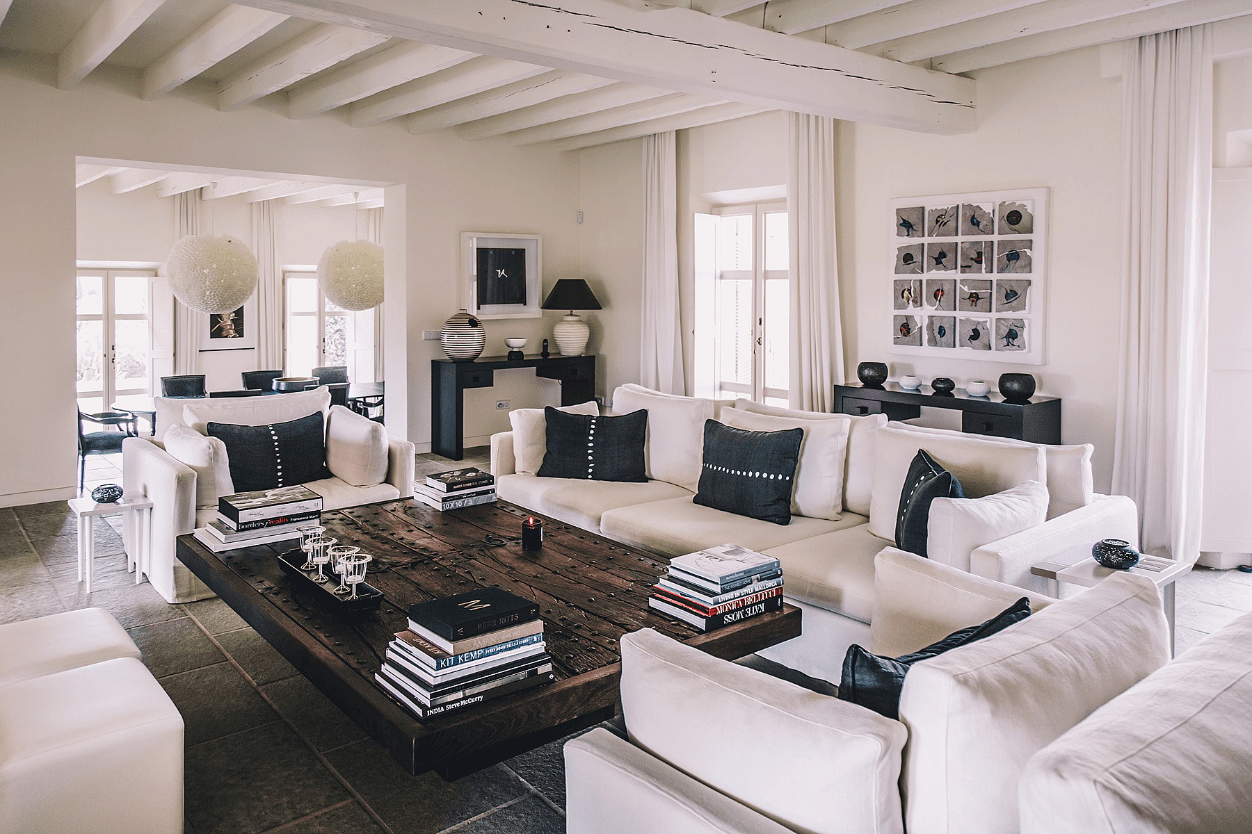Spacious living room featuring white sofas, a dark wood coffee table, and exposed white-painted wooden ceiling beams.