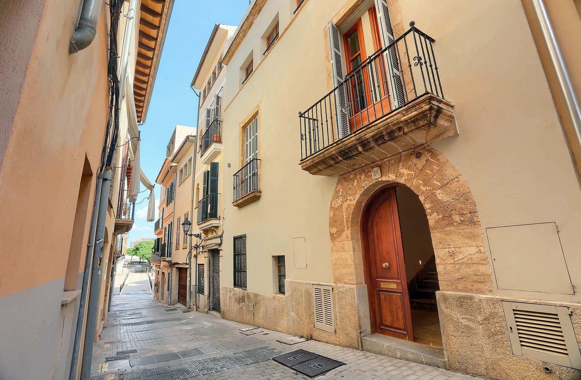 Exterior view of a multi-story townhouse in a narrow cobblestone street, featuring a stone arched entrance and iron balcony.