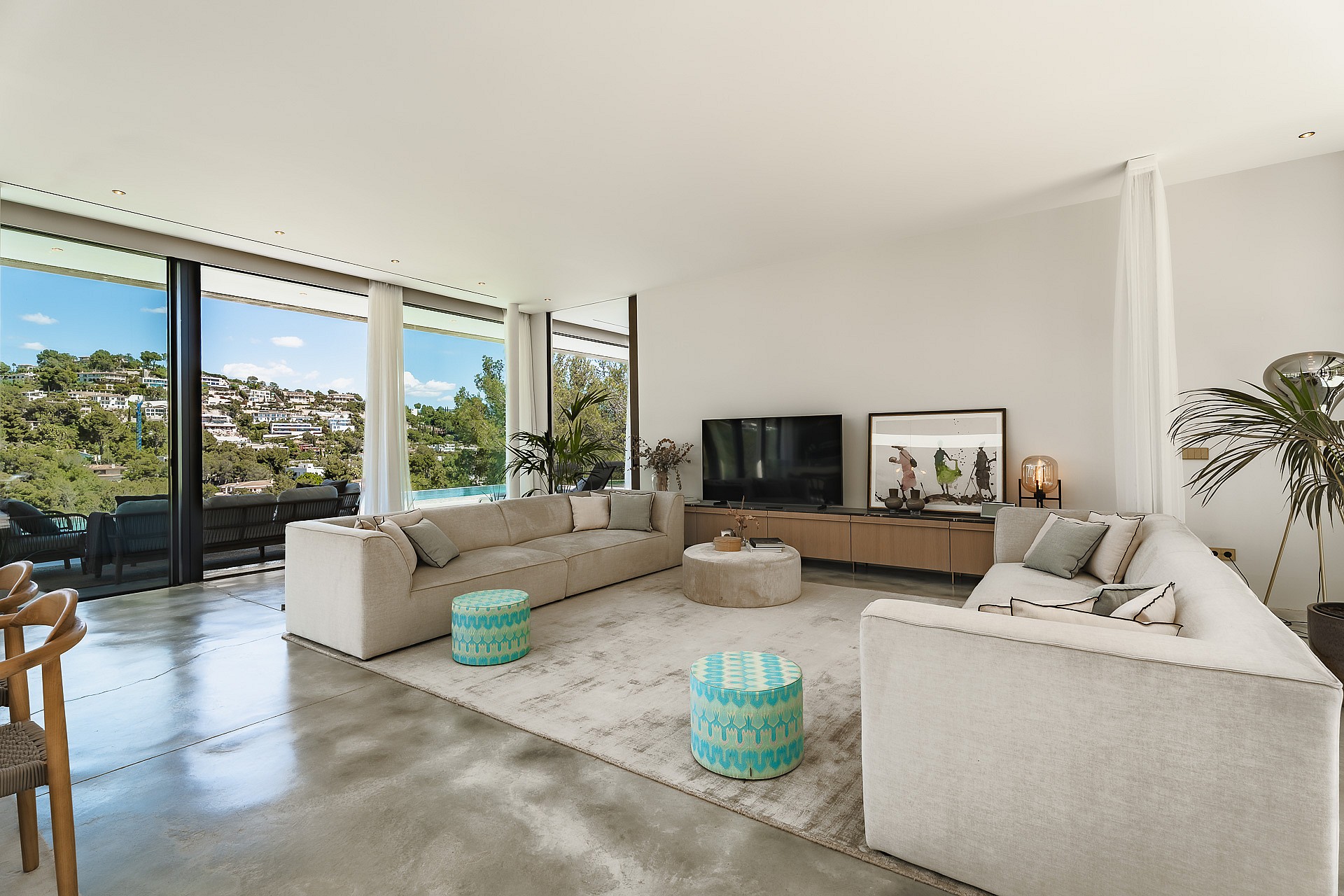 Modern living room with polished concrete floors, modular sofas, and full-height glass doors overlooking the hills.