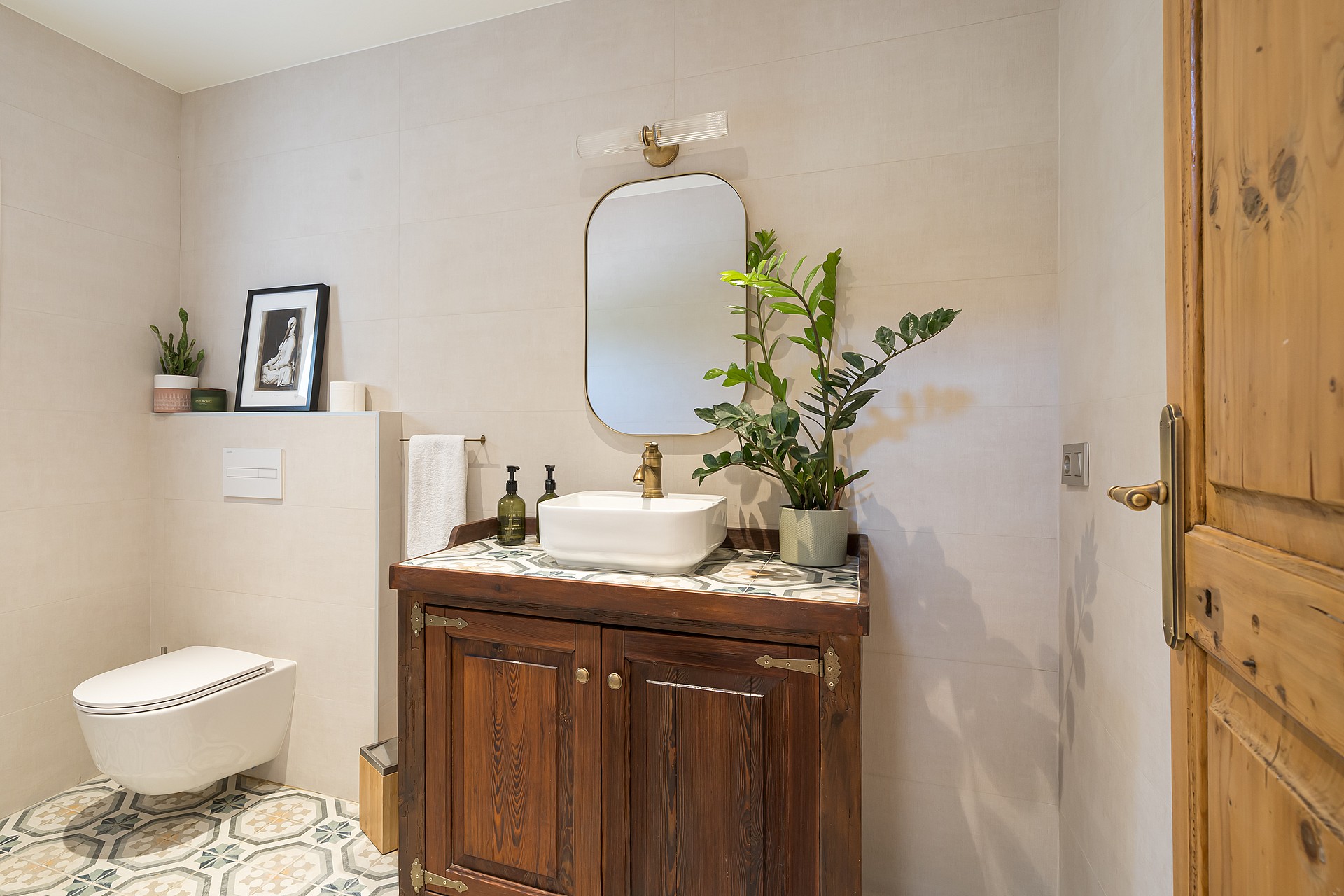 A bathroom featuring a dark wood vanity cabinet, white vessel sink, patterned floor tiles, and a wall-mounted toilet.