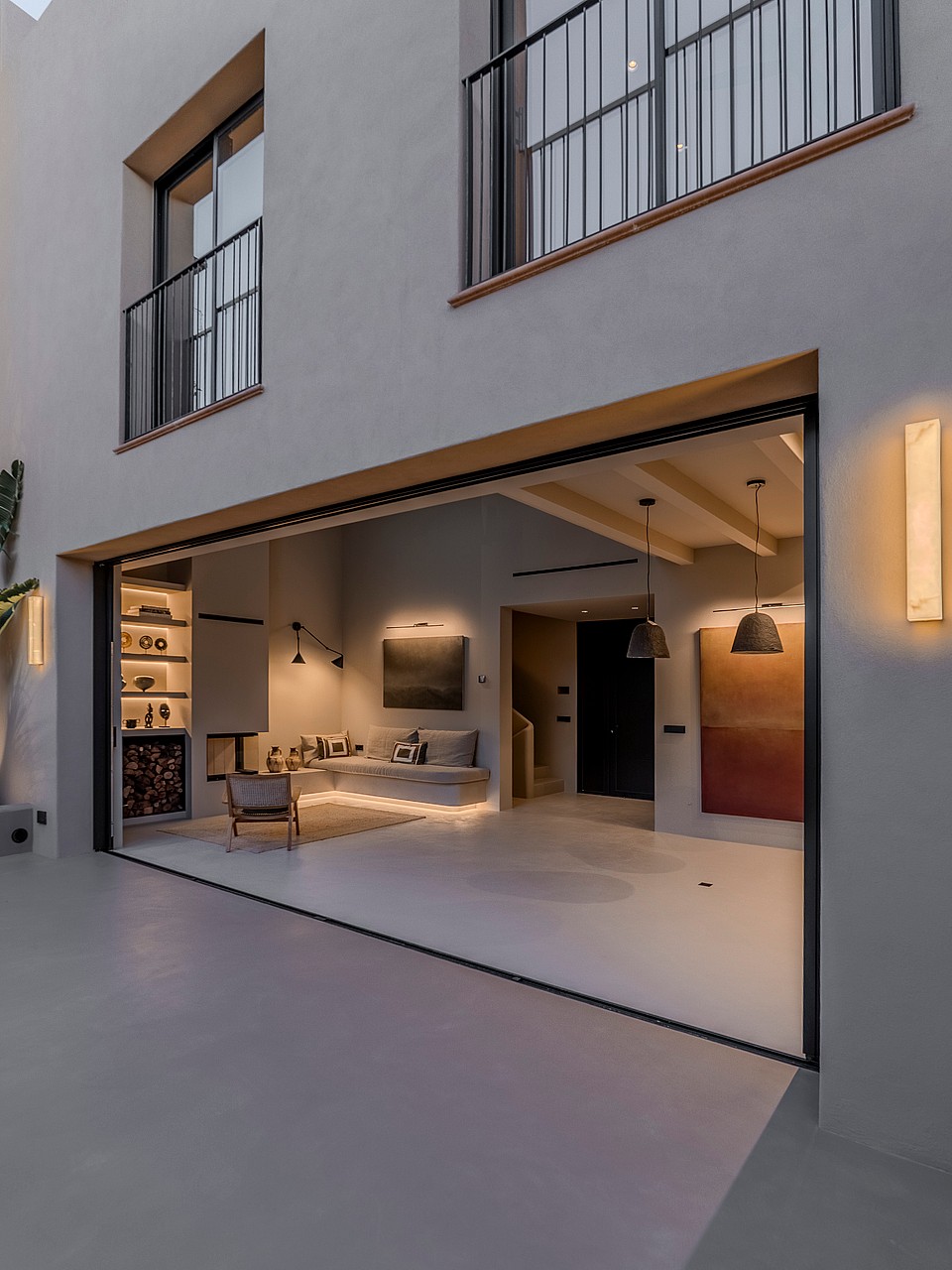 Exterior shot of a white townhouse facade with wide sliding doors revealing an interior with wood beams and a fireplace.