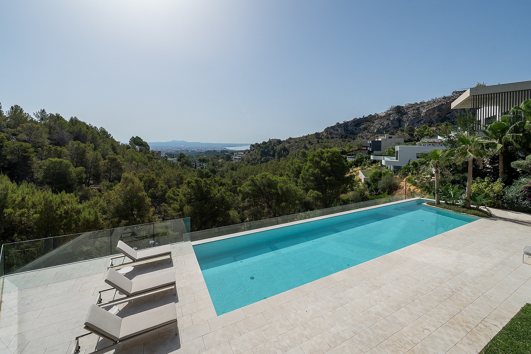 Rectangular swimming pool with clear blue water and stone deck, set against a backdrop of forested hills and distant sea.