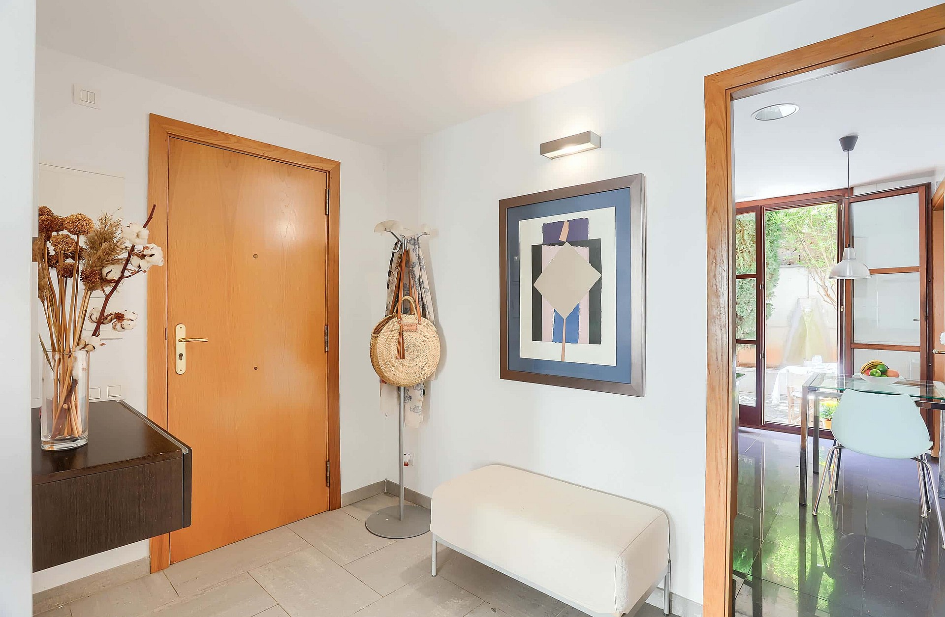 Entrance foyer featuring a light wood door, an upholstered bench, wall-mounted art, and a view into the dining area.