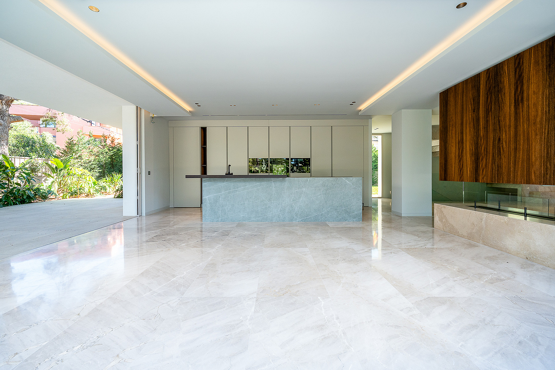 Wide shot of a modern kitchen with a blue-grey stone island, polished light-colored marble flooring, and a linear fireplace.