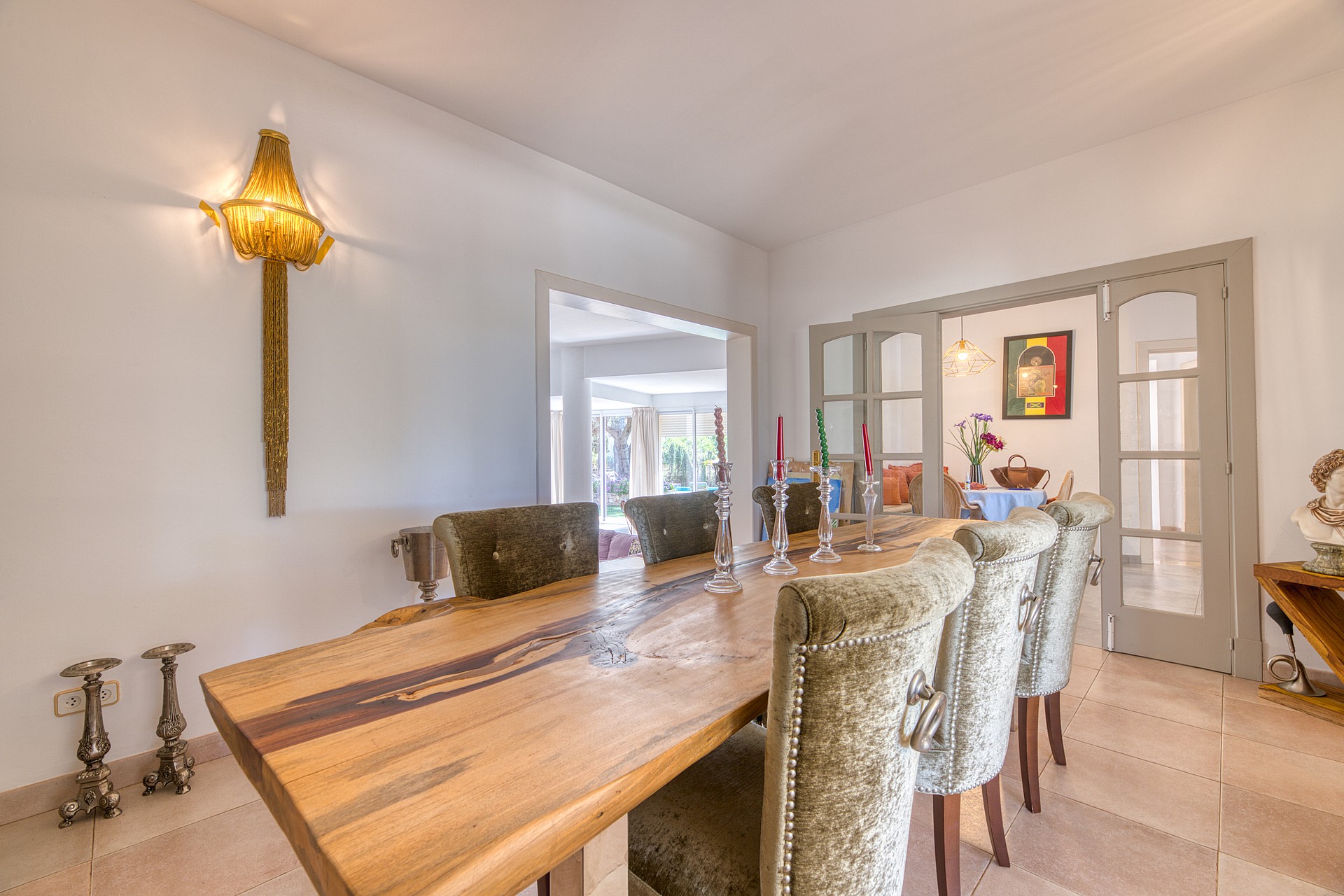 A formal dining room featuring a long live-edge wooden table, upholstered high-back chairs, and neutral stone tile floors.