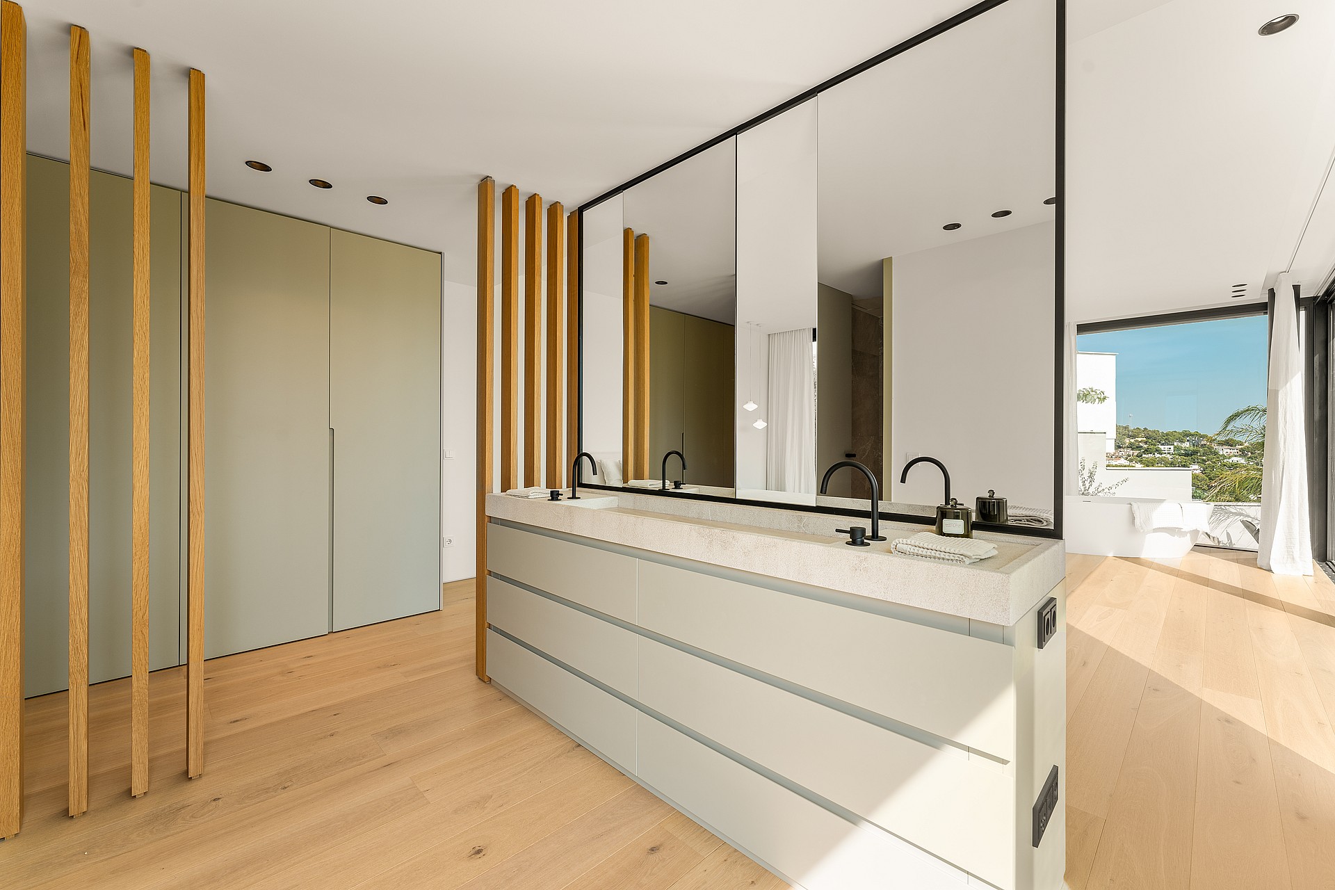 Modern master bathroom featuring a dual vanity with white stone countertop, black faucets, a large mirror, and light oak floors.