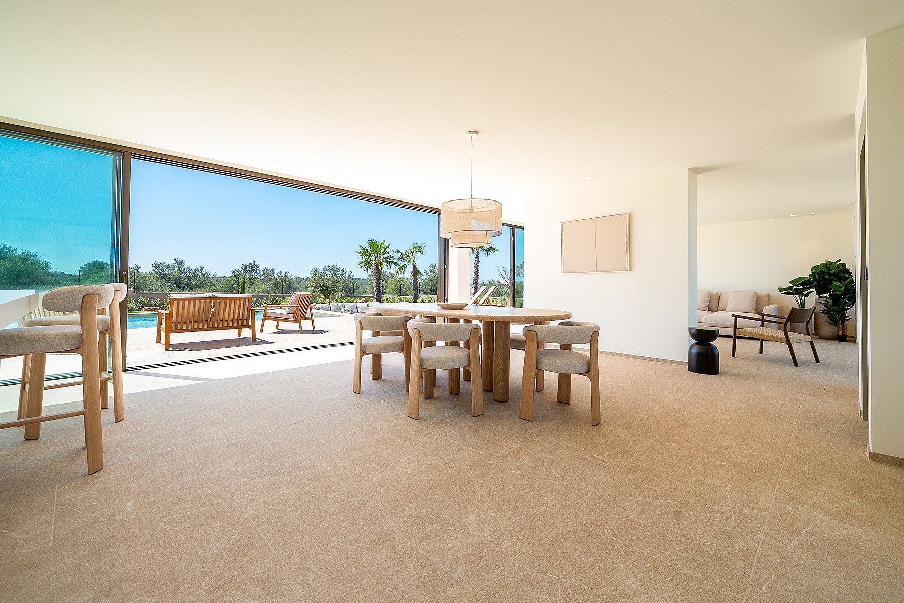 Dining room with circular wooden table and upholstered chairs, opening to a terrace with mountain views in Son Gual.