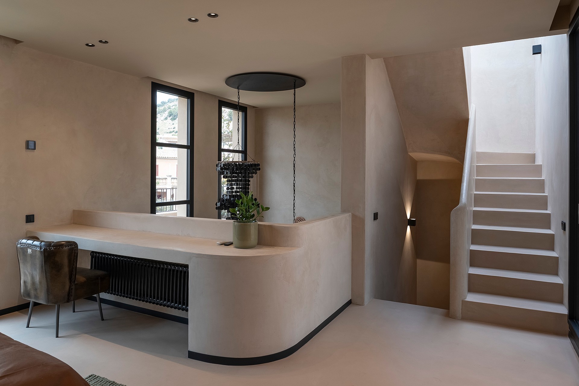 A minimalist home office area with a curved plaster desk and a stone staircase in a neutral, modern townhouse interior.