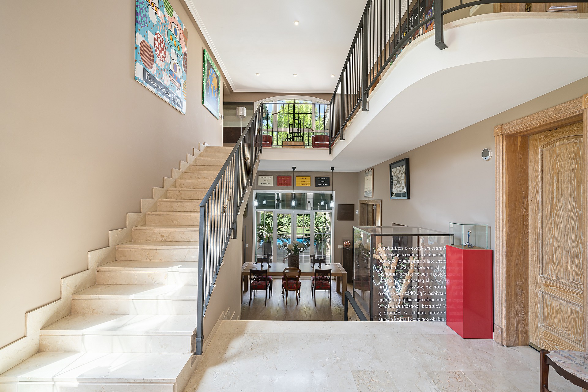 An expansive entrance hall with a polished stone staircase and ornate metal railings, looking towards a dining area beyond.