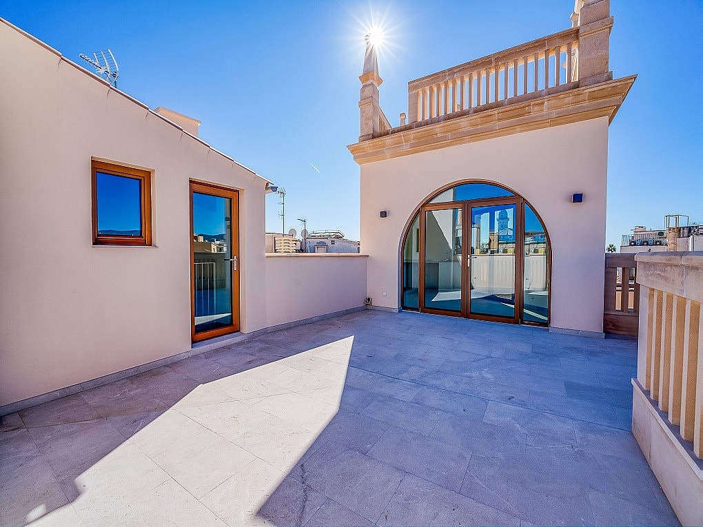 A sunny rooftop terrace with light-colored stone flooring, an arched glass door, and traditional architectural detailing.