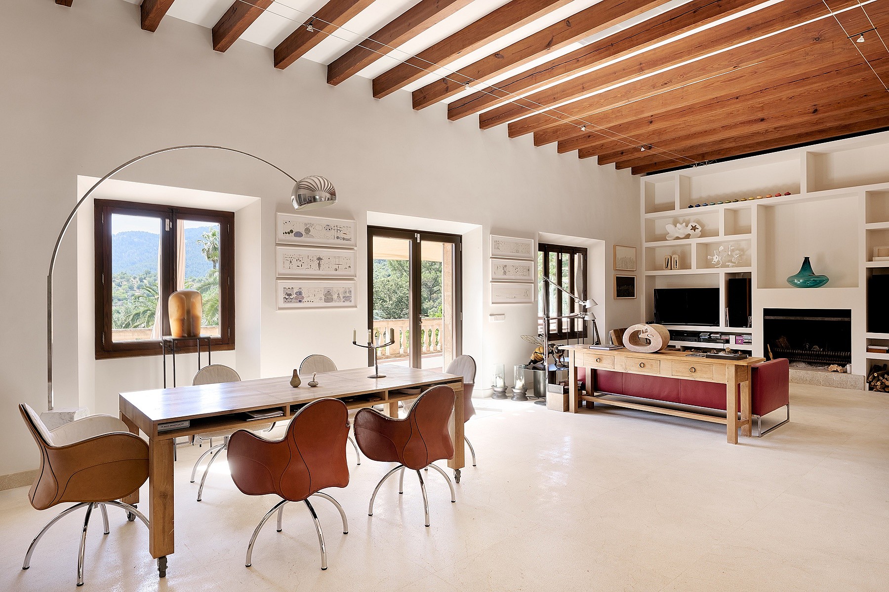 Spacious living room with exposed wood ceiling beams, white plaster walls, dining table with leather chairs, and fireplace.