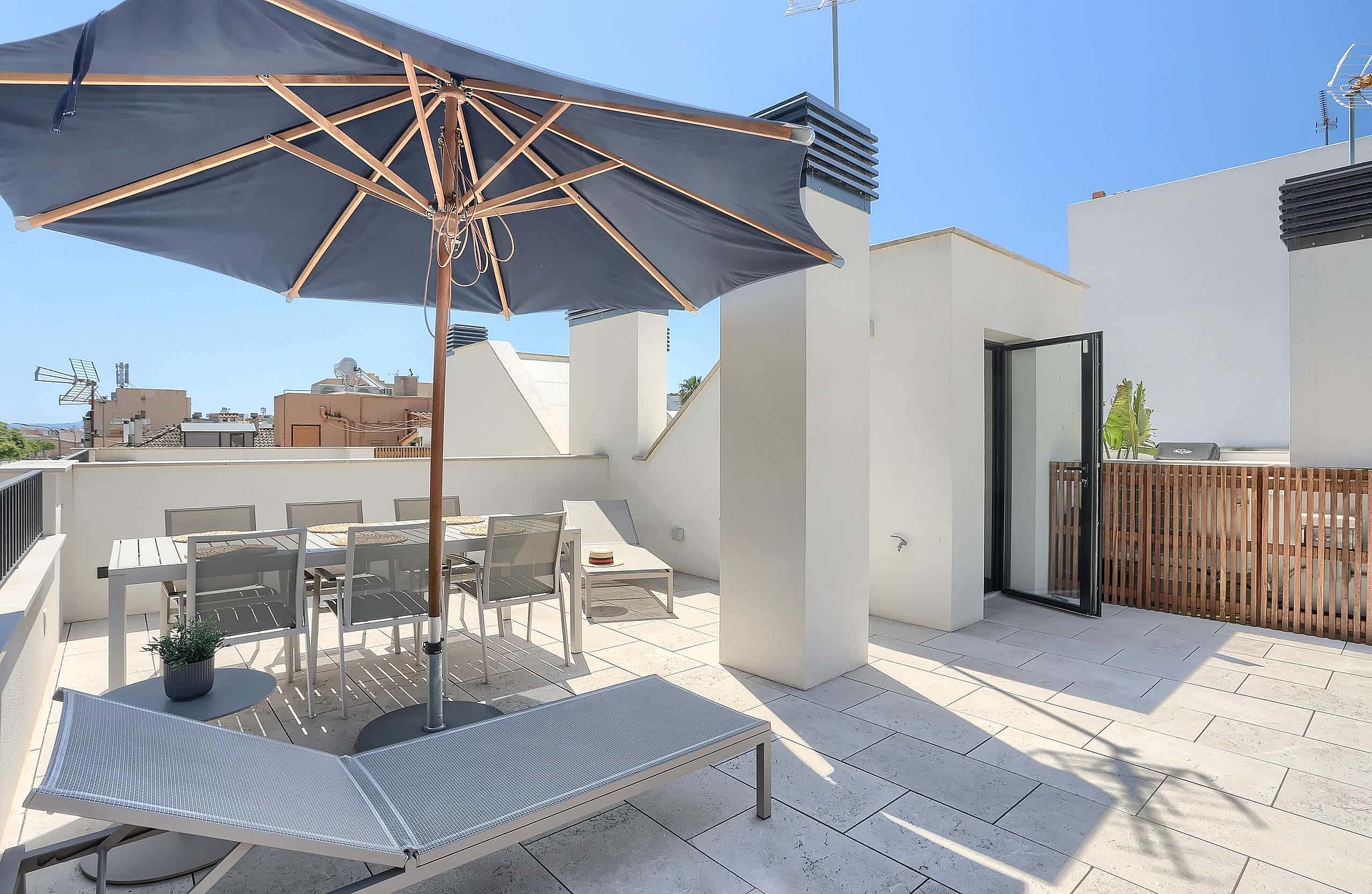 Rooftop terrace in El Molinar featuring a dining set under a grey parasol, sun loungers, and white stone flooring.