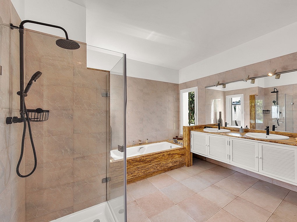 Modern bathroom featuring a glass-enclosed walk-in shower with matte black fixtures, a white soaking tub, and a wooden vanity.