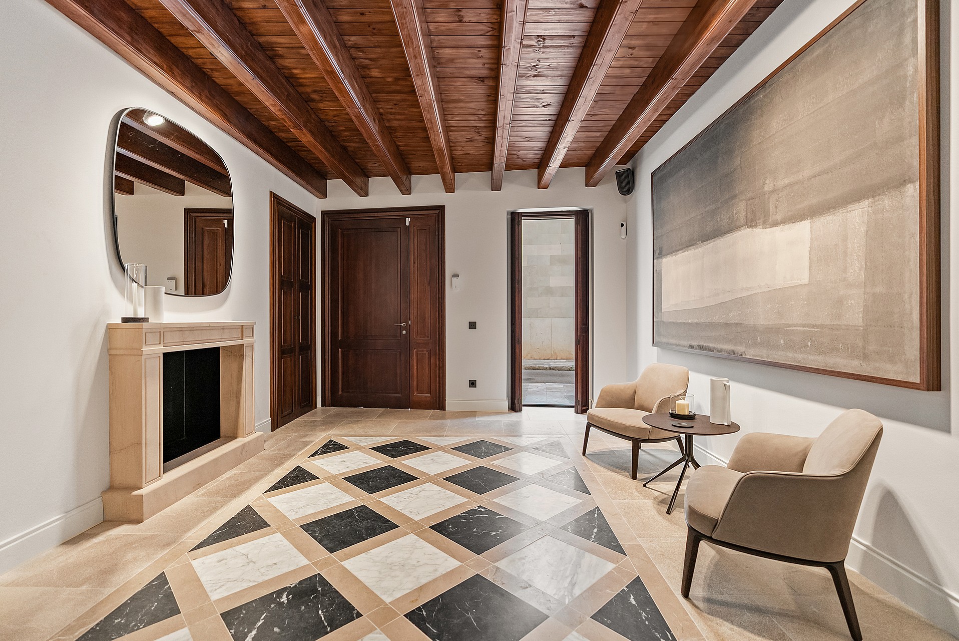 Grand entrance hall featuring dark wood ceiling beams, a checkered marble floor, and a stone fireplace with an organic mirror.