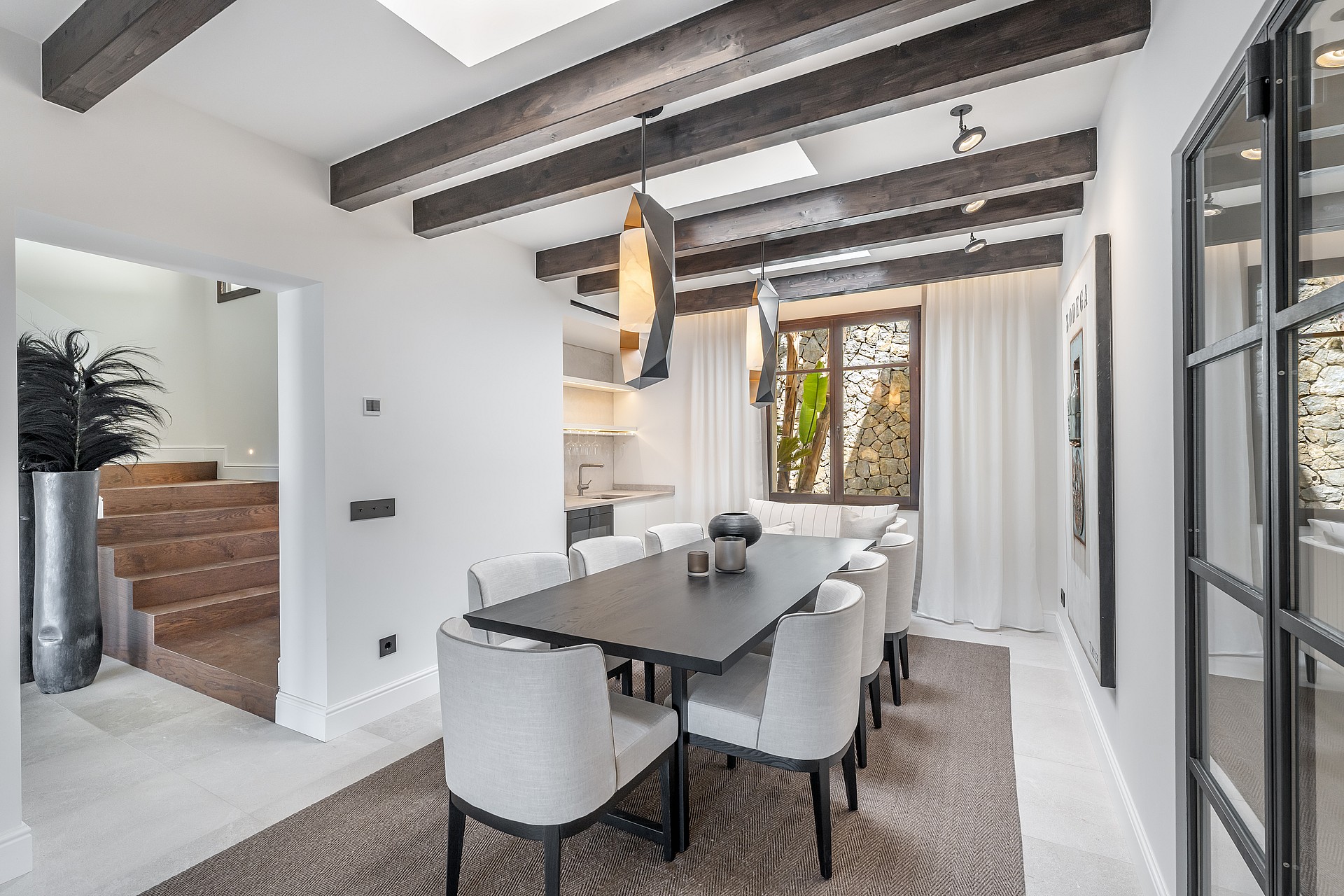 Modern dining room featuring a dark wood table, grey upholstered chairs, exposed ceiling beams, and integrated skylights.
