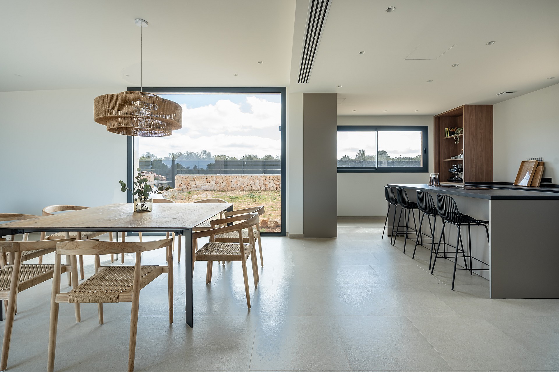 A modern, open-plan dining and kitchen area with polished concrete floors, wooden furniture, and mountain views through windows.