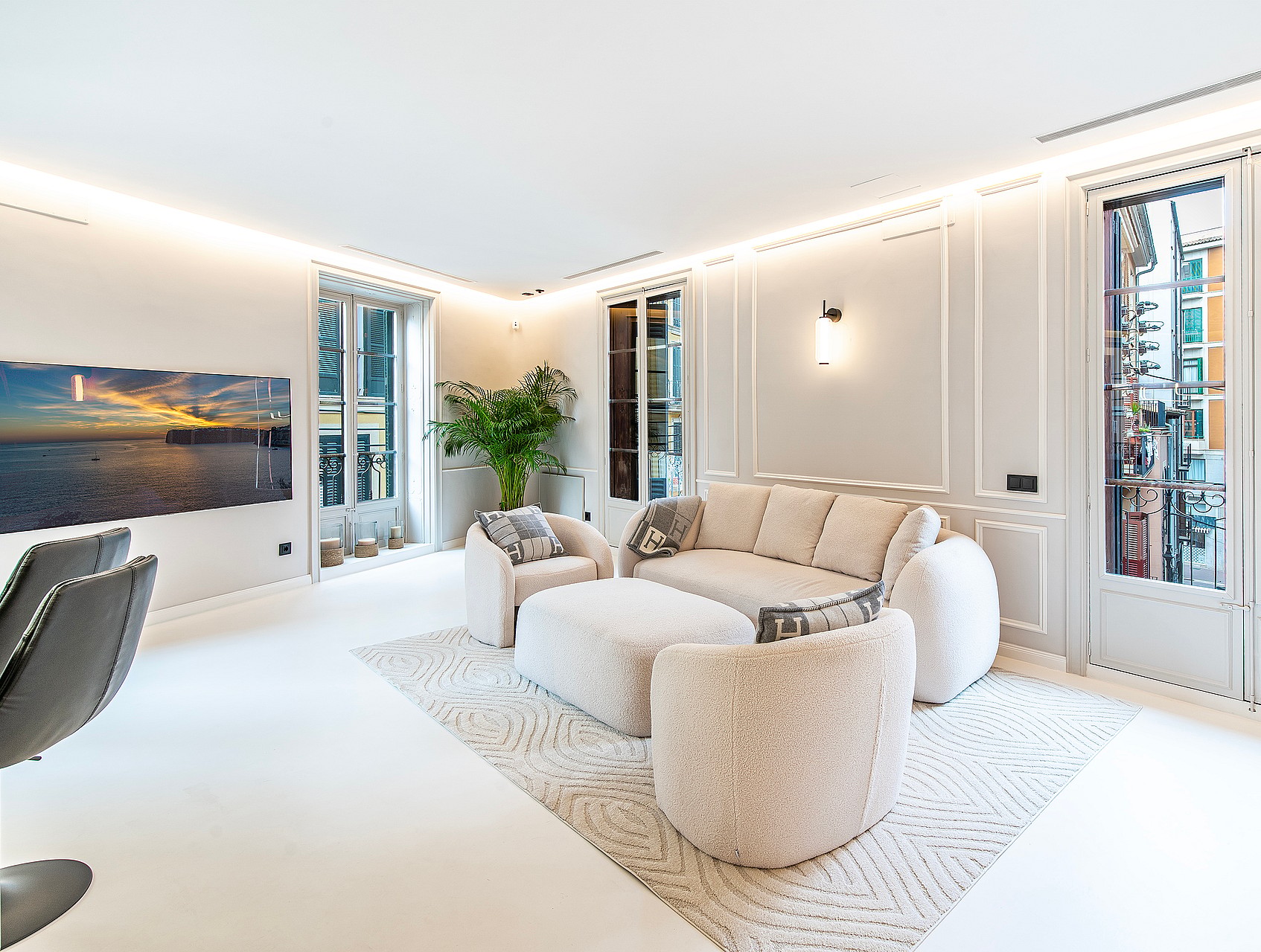 A bright, modern living room featuring cream-colored textured armchairs, a large sofa, and white walls with vertical paneling.