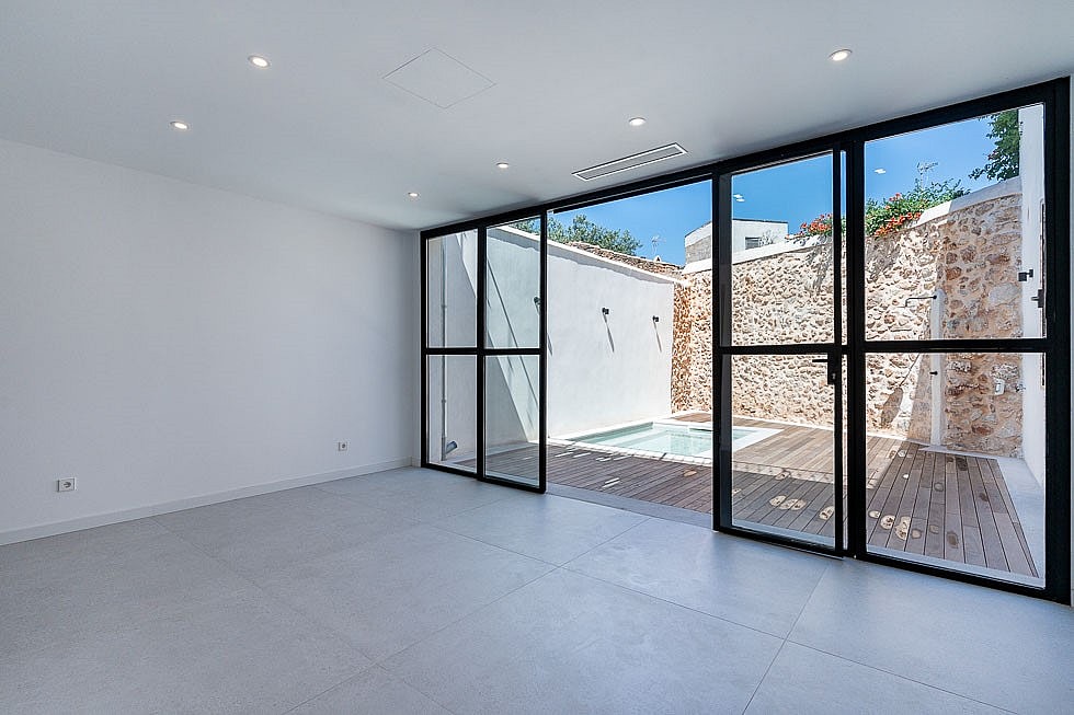 Modern interior living space featuring white walls, large black-framed glass sliding doors, and a view of a small pool.