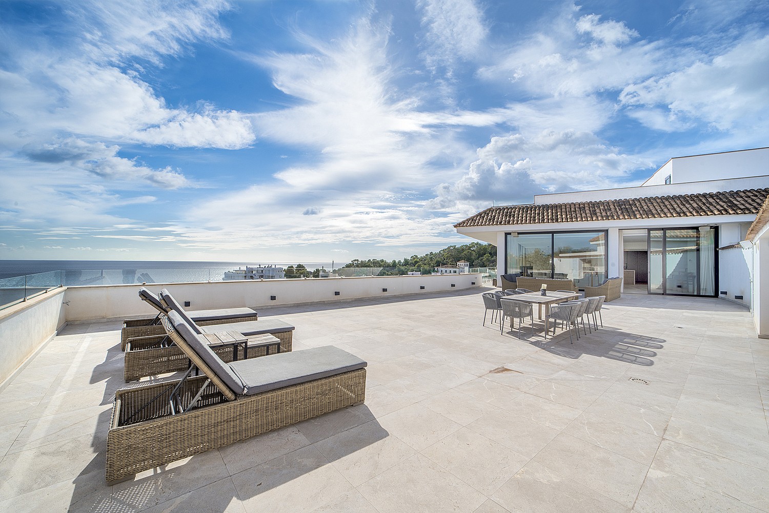 A wide outdoor terrace in Illetas featuring sun loungers, an outdoor dining table, and direct views of the Mediterranean sea.