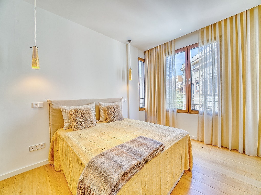 A double bedroom featuring wooden floors, beige curtains, and two hanging pendant lights beside the bed headboard.