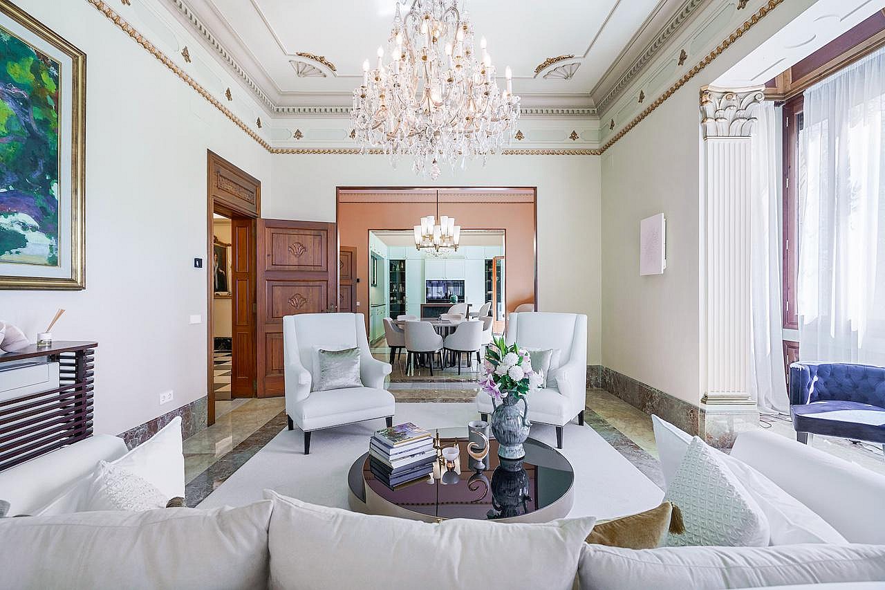A formal living room with cream walls, detailed crown molding, a crystal chandelier, and view through to the dining area.