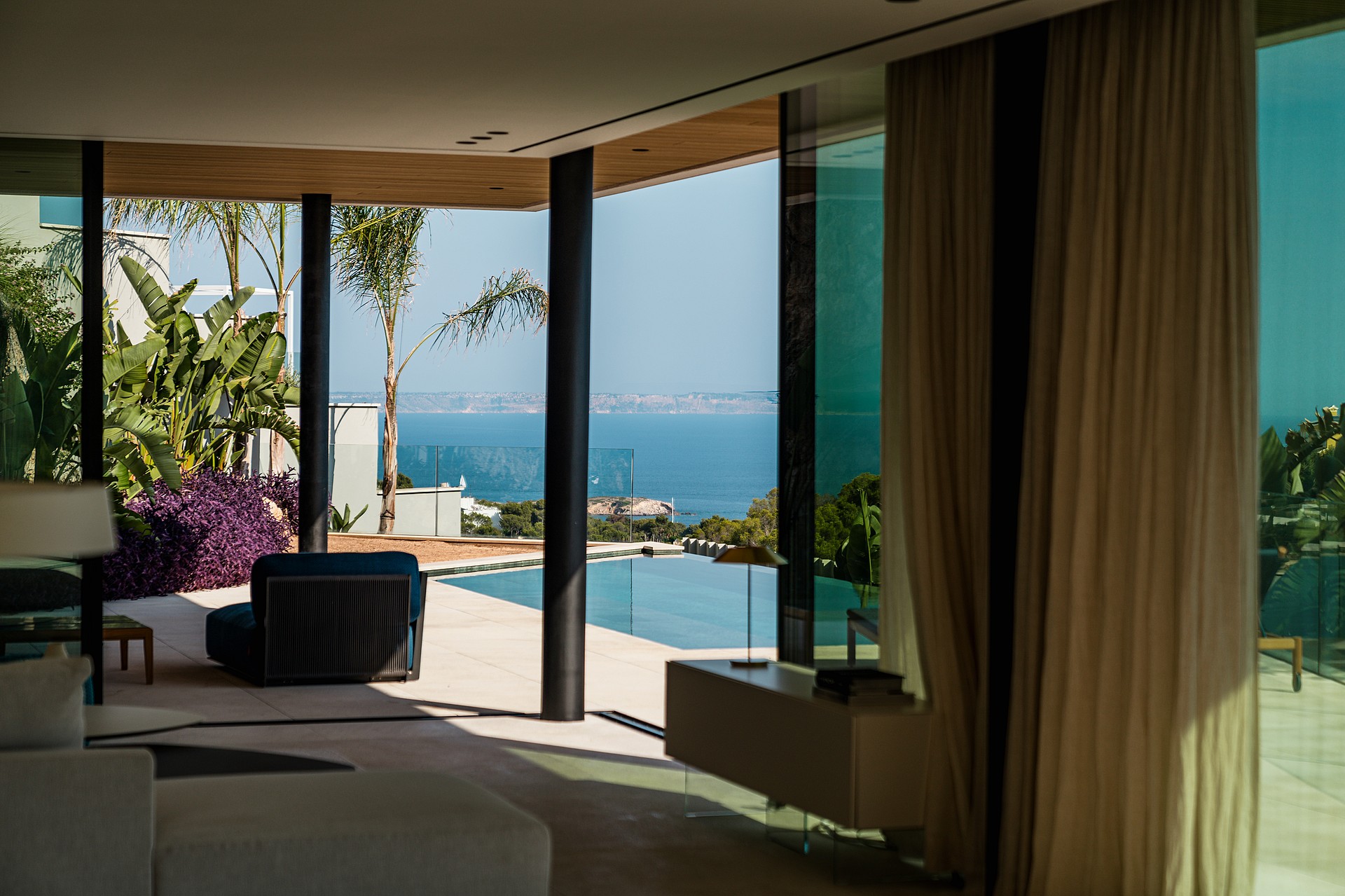 An interior living space looking out toward a swimming pool and the Mediterranean sea through large glass walls.