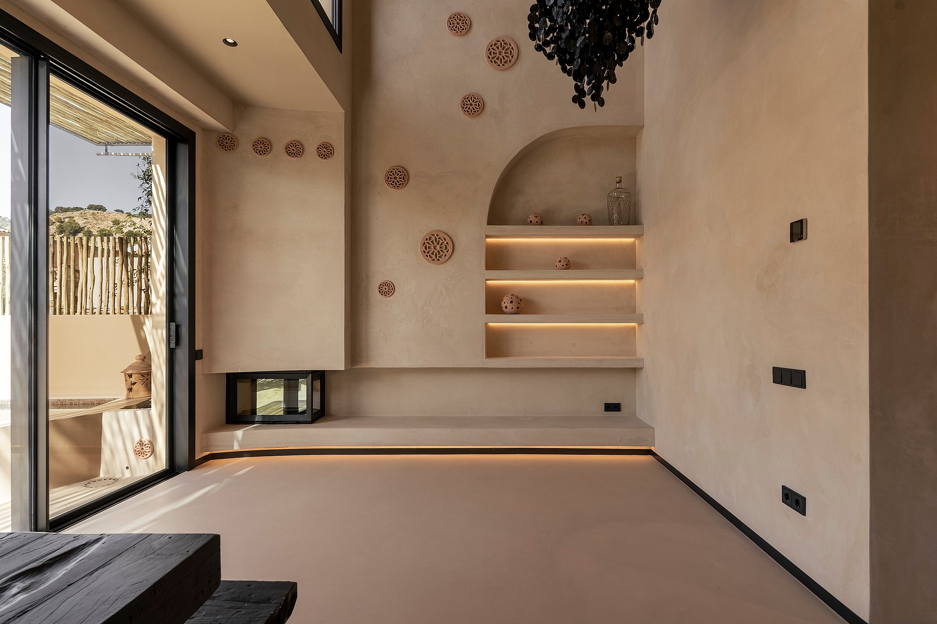 Empty living room with textured beige walls, built-in arched stone shelves, recessed lighting, and large sliding glass doors.