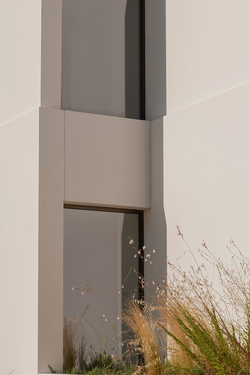 A close-up of a contemporary building exterior with geometric stone panels and a vertical recessed glass window.