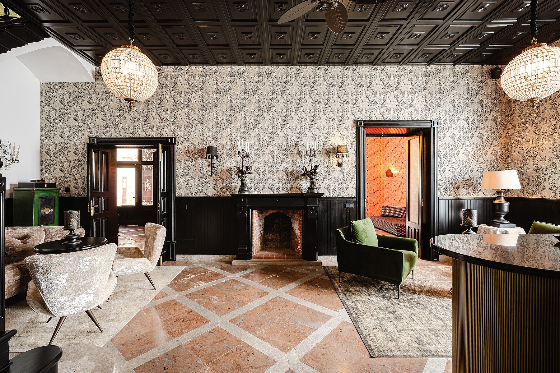 A formal living area featuring intricate patterned wallpaper, a black coffered ceiling, and a central stone fireplace.