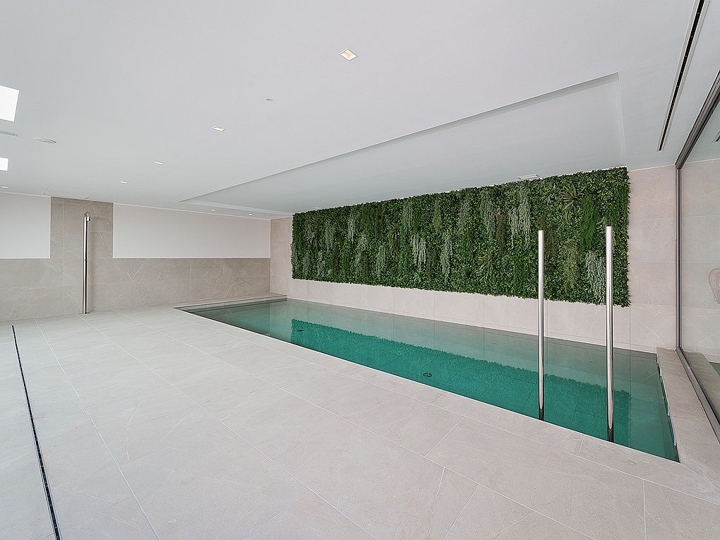 Piscina interior con agua turquesa, barandillas de acero y gran jardín vertical sobre suelo de piedra gris.