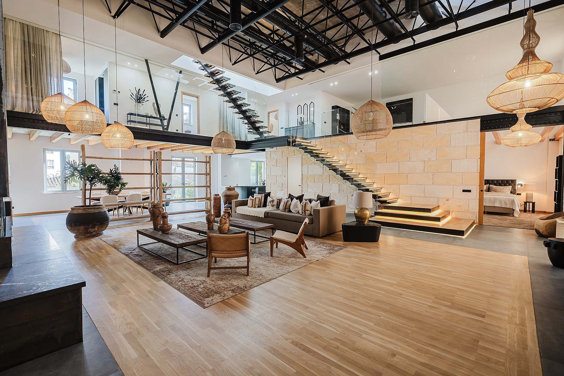 Double-height living space with light wood floors, a natural stone feature wall, and a dramatic steel staircase.