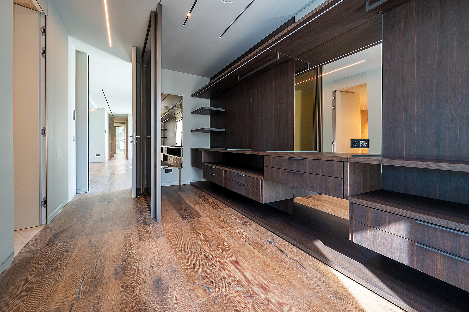 A modern walk-in closet with dark wood storage units, integrated LED lighting, and light-toned oak hardwood flooring.