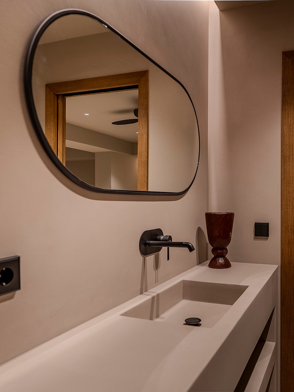 A contemporary bathroom detail featuring an integrated stone sink, a matte black wall-mounted faucet, and an oval mirror.