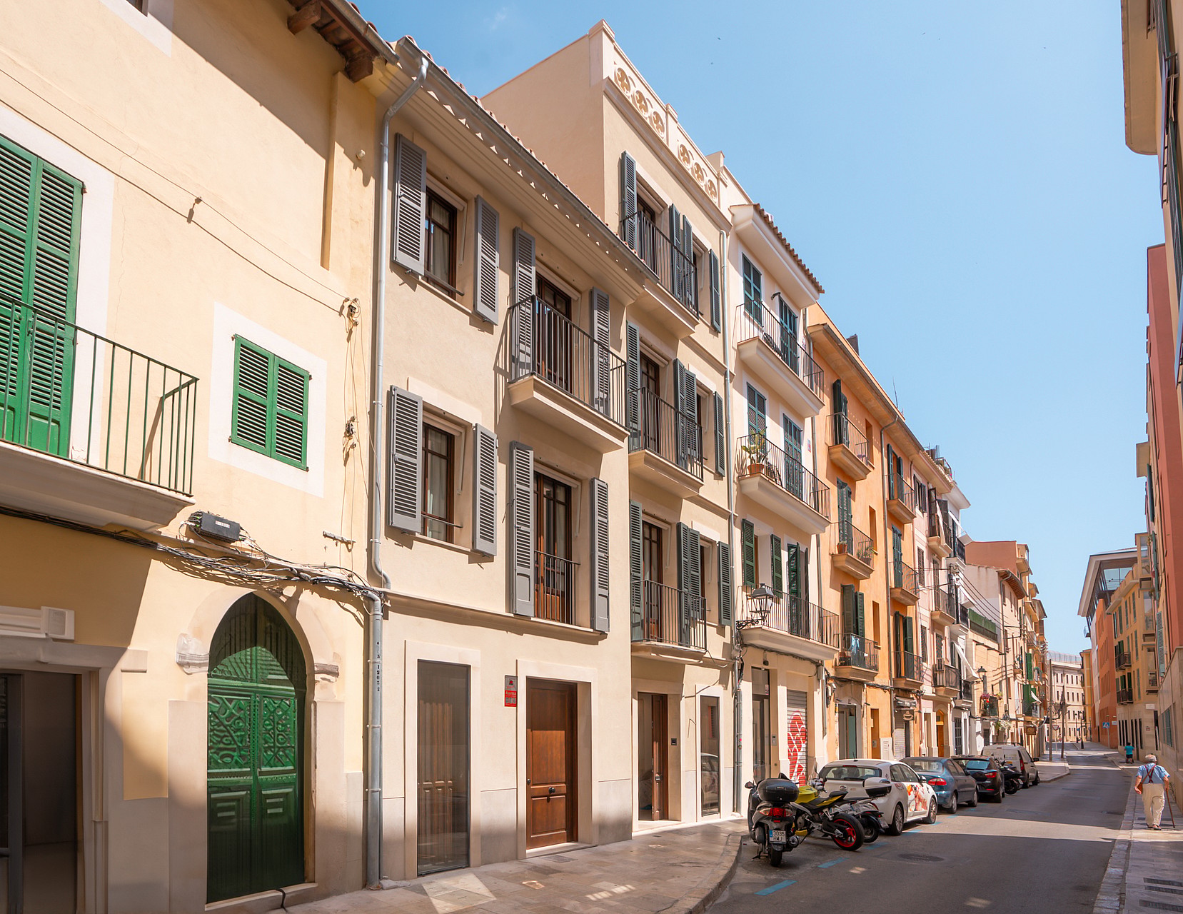 Multi-story Mediterranean townhouses featuring sand-colored plaster, green wooden shutters, and wrought-iron balconies.