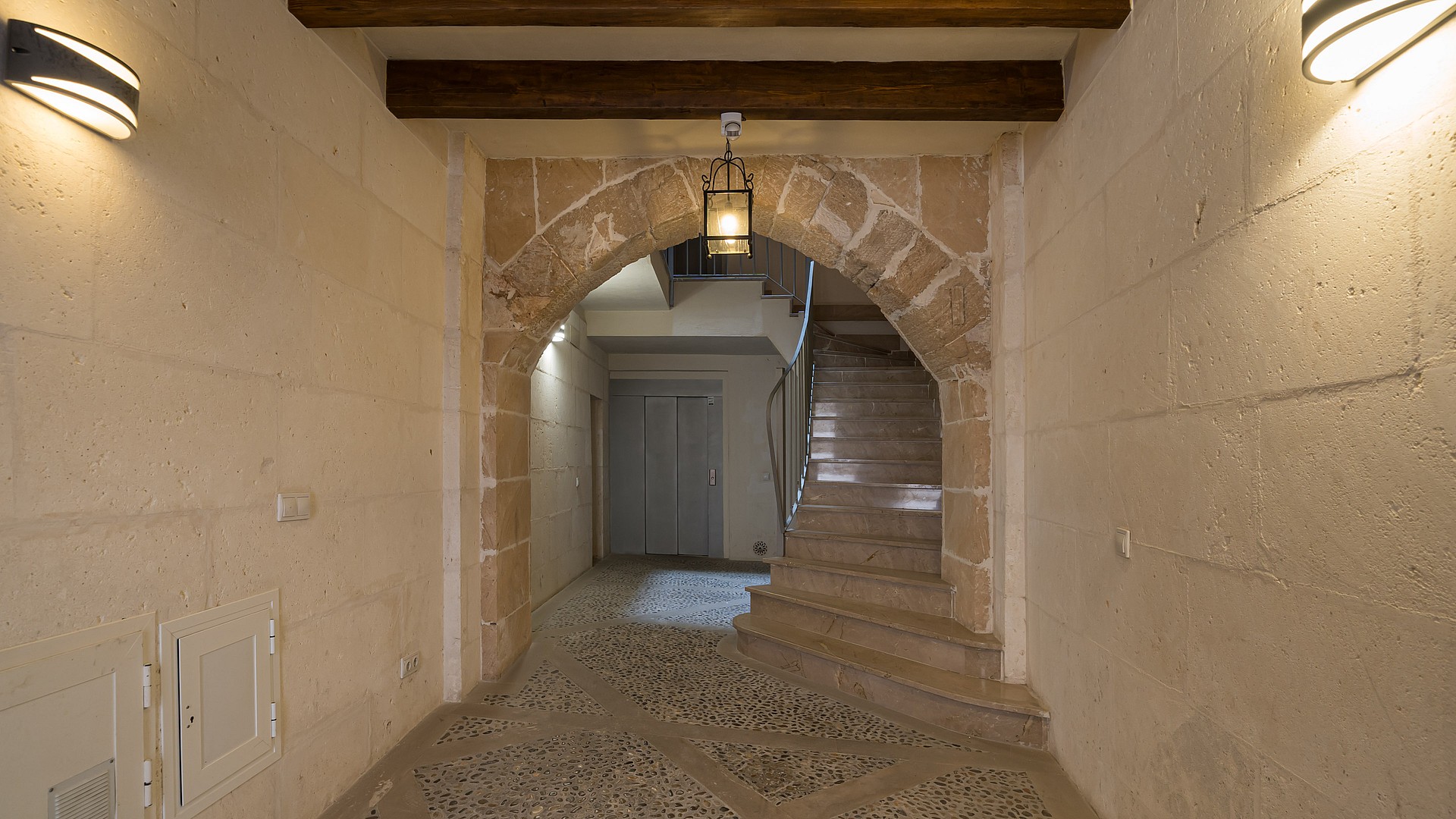 Entry hall featuring a traditional stone arch, exposed wooden beams, and pebble flooring in an 18th-century building.