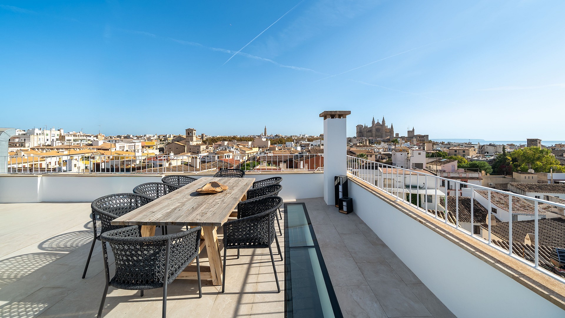 Expansive rooftop terrace with a wooden dining set overlooking the Palma city skyline and Cathedral under a clear blue sky.