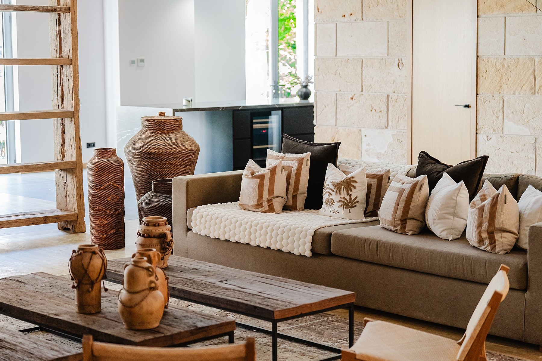 Interior view of a living room featuring a textured stone wall, a neutral sofa with decorative cushions, and rustic wooden decor items.