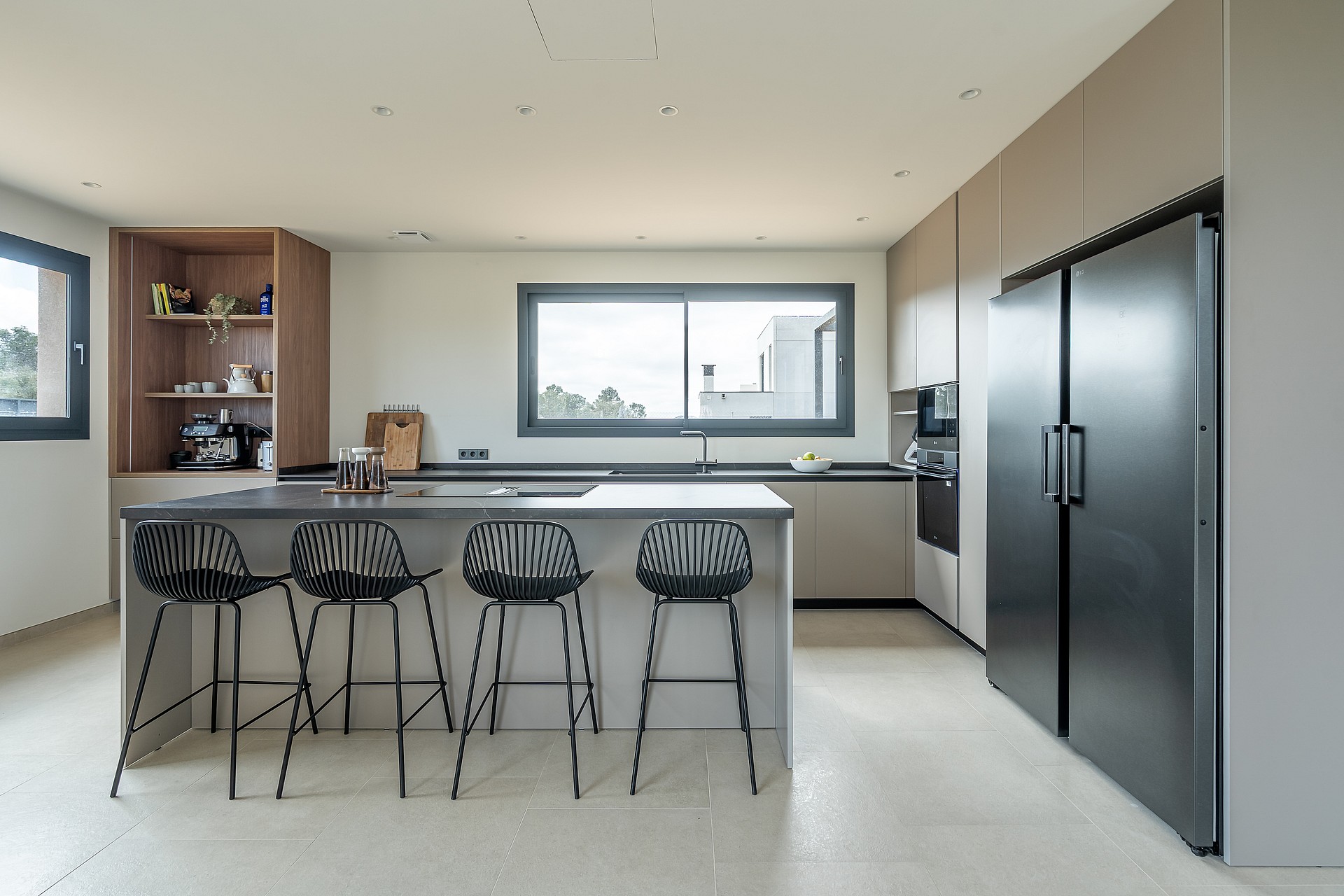 Modern open kitchen with light grey cabinetry, black refrigerator, and a central island with four black wire stools.