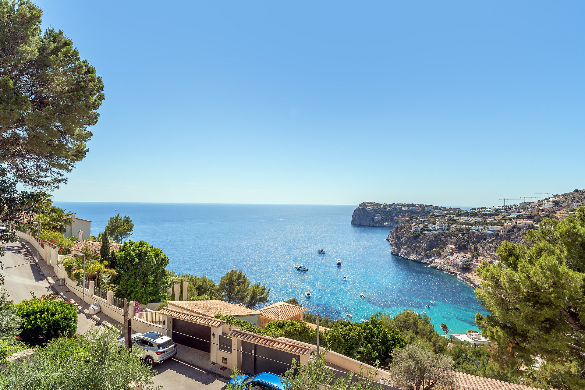 Elevated perspective of a coastal residential street overlooking the blue Mediterranean sea with several small boats.