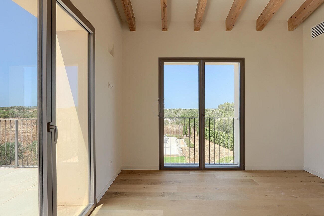 Unfurnished bedroom with wooden beamed ceiling, oak flooring, and glass doors opening to a private balcony with mountain views.