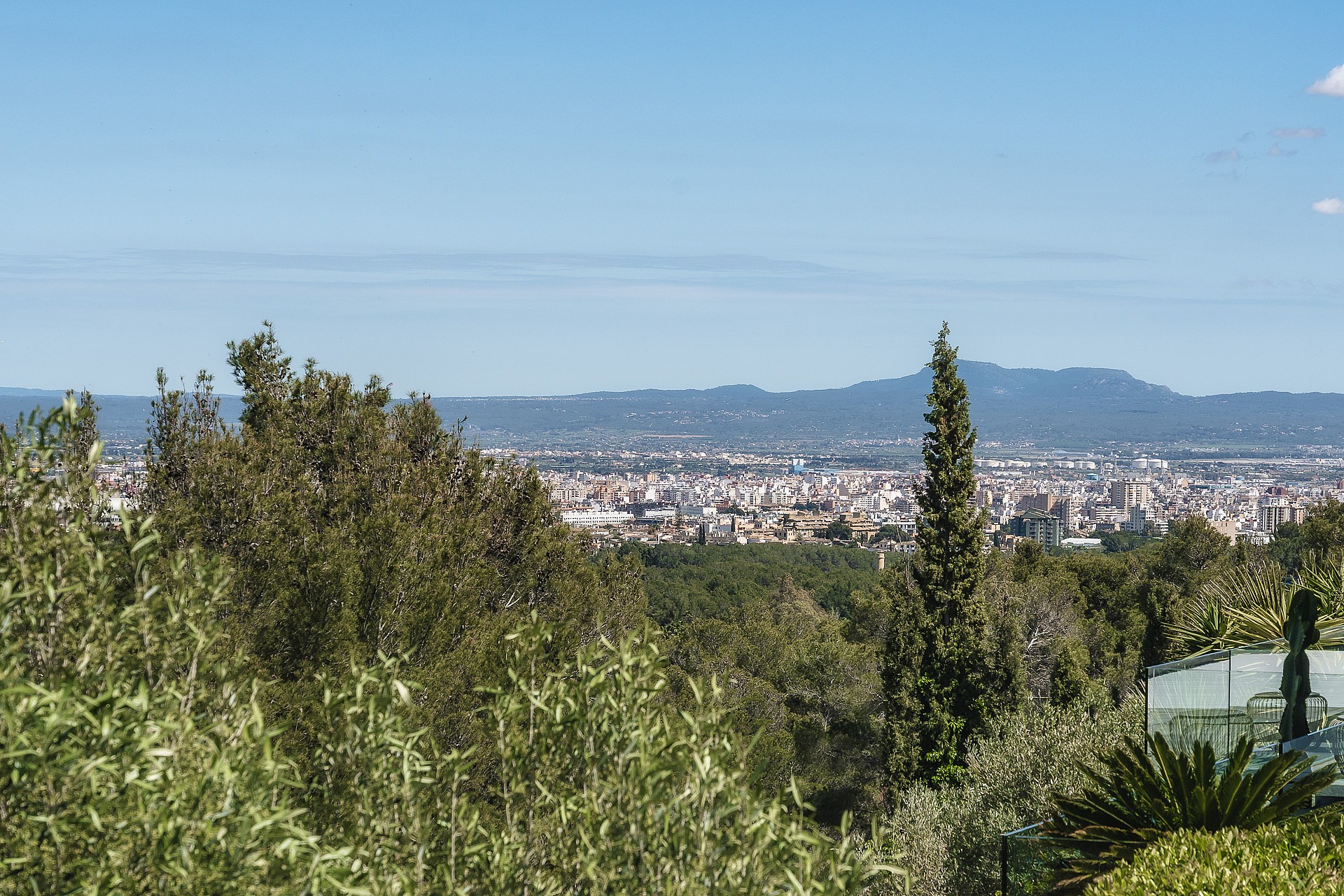 Elevated view from a Son Vida villa overlooking the Palma city skyline with distant blue mountains and lush greenery.