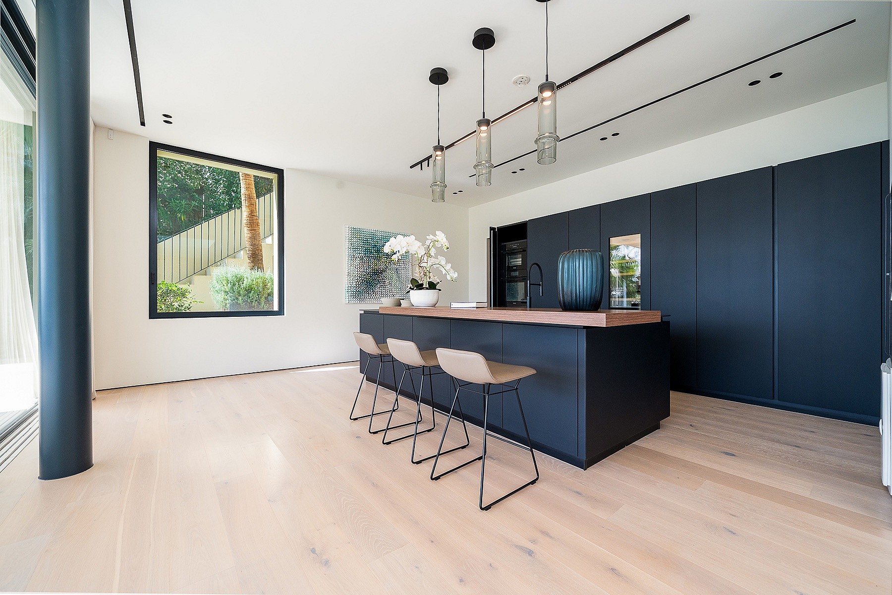 Modern open-plan kitchen featuring a dark matte island, light oak hardwood floors, and three pendant lights in Son Vida.