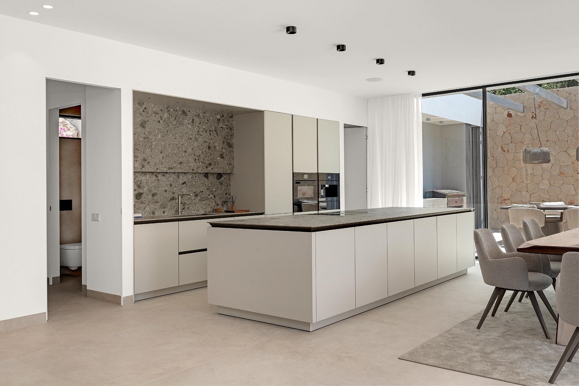 Handleless island kitchen with dark stone worktop, terrazzo-effect splashback and garden views