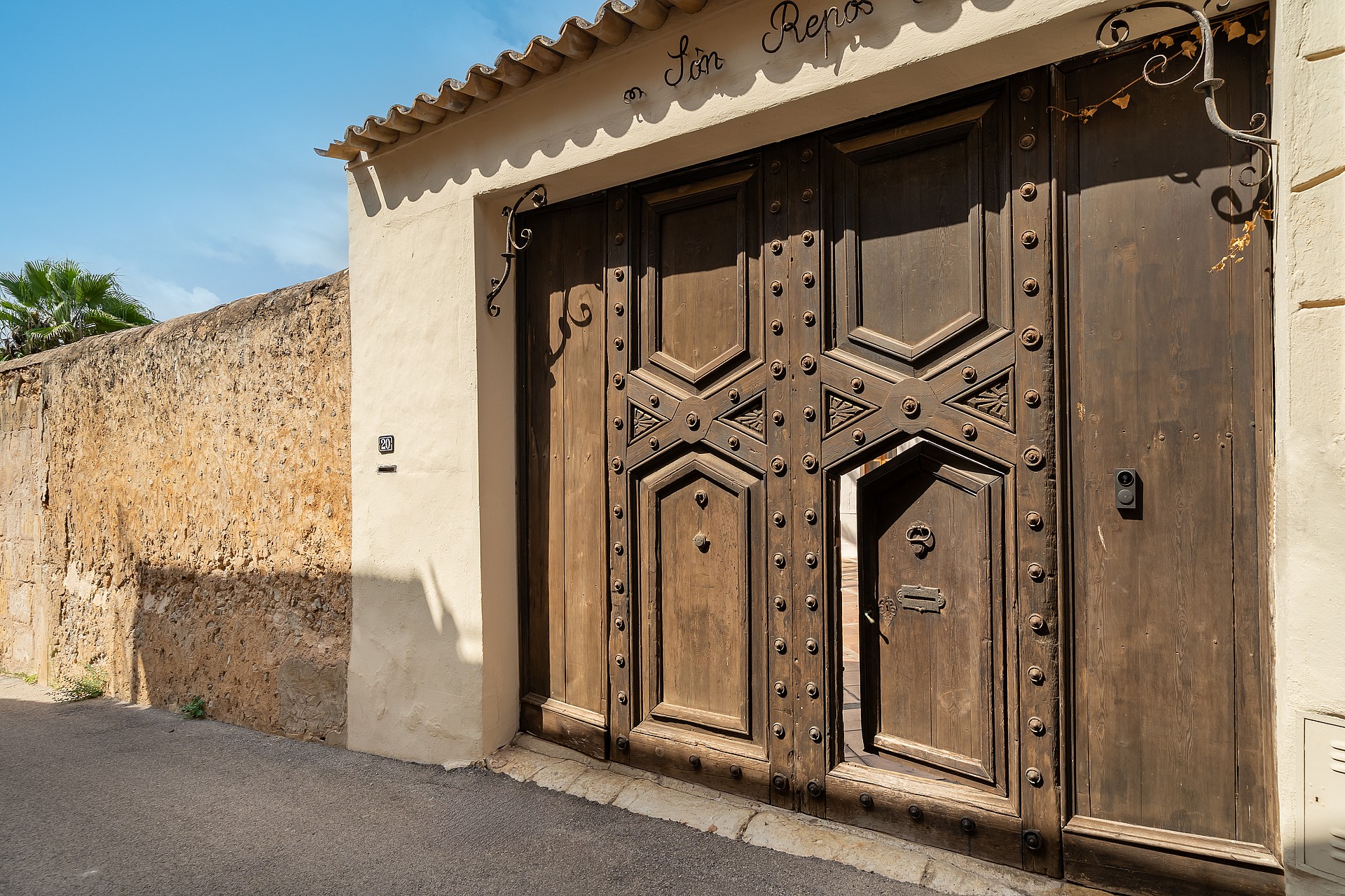 Heavy dark wood gate with iron studs and an inset pedestrian door set into a stone wall under tiled eaves.