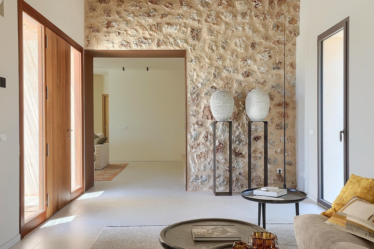 Interior view of an entrance hall featuring a tall dry stone wall, wooden doors, and two sculptural vases on metal stands.
